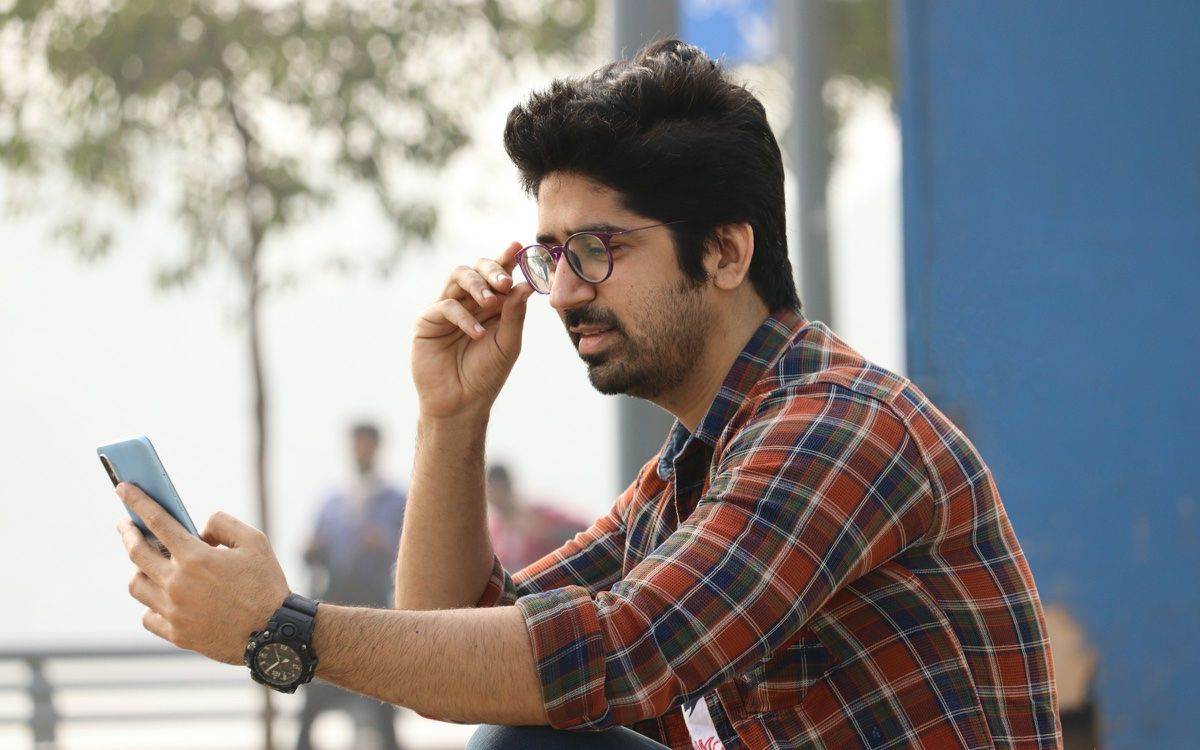 A young man in glasses checking his phone outdoors